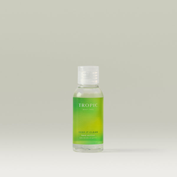 A clear bottle of Tropic Body Care ‘Keep It Clean’ hand sanitiser with a green label and white flip-top cap, standing against a soft neutral background.