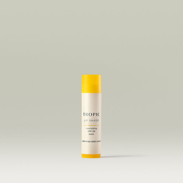 A tube of Tropic Lip Shade nourishing SPF 50 balm with a yellow cap and white body, labelled 'Certified Reef-Safe,' standing upright on a neutral background.