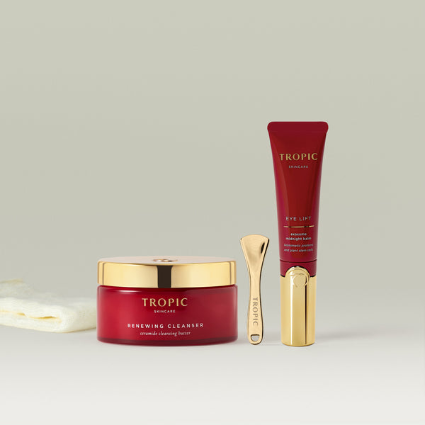 Tropic Renewing Cleanser and Eye Lift balm with gold spatula displayed on a clean, minimal background with a soft cloth beside them.