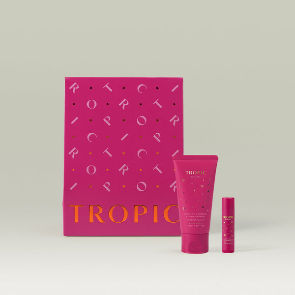 Tropic Skincare gift set titled The Soft Touch Treatment – hand and lip duo, featuring a limited-edition Passion Flower & Pink Pepper hand cream and matching lip love, displayed in front of a vibrant pink gift box with metallic detailing.