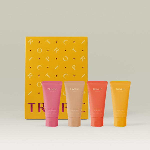 Tropic Skincare gift set titled Tropical Showers – transportive body wash set, featuring four colourful body washes: Tahiti Blooms, Vanilla Amber, Mango Grove, and Signature, displayed in front of a vibrant yellow gift box.