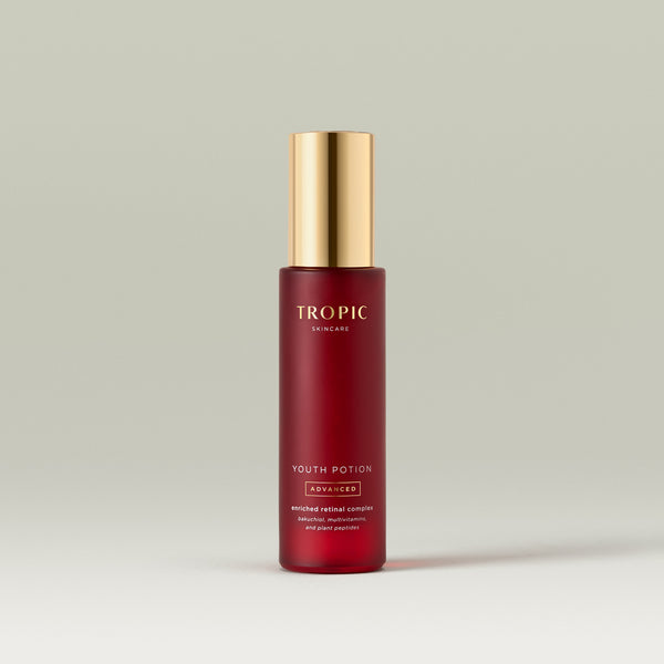 Red glass bottle of Tropic Youth Potion Advanced serum with gold pump cap on a neutral background